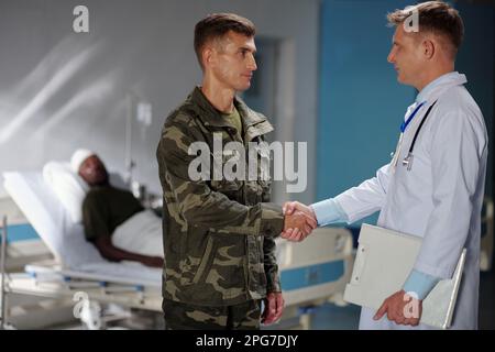 Soldat in Uniform schüttelt Hand mit Arzt und diskutiert Gesundheitszustand des Patienten im Krankenhaus Stockfoto