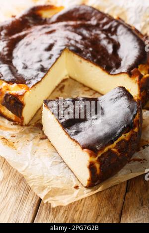 Frische und köstliche hausgemachte baskische Käsekuchen auf dem Pergamentpapier auf dem Holztisch. Vertikal Stockfoto