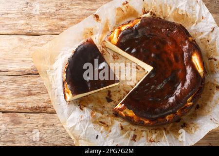 Rustikaler, frischer und köstlicher baskischer Käsekuchen als Nahaufnahme auf dem Pergamentpapier auf dem Holztisch. Horizontale Draufsicht von oben Stockfoto