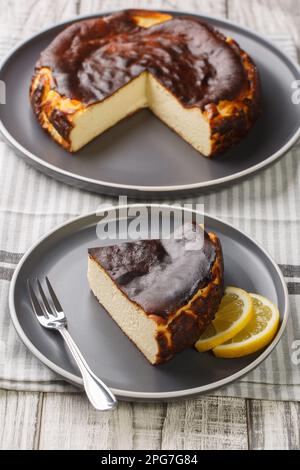 Zart geschnittener, cremig verbrannter baskischer Käsekuchen mit Zitronenkeilen auf einem Teller auf dem Tisch. Vertikal Stockfoto