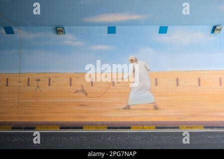 Bemalte Überführung auf der Straße. Es zeigt einen Mann im traditionellen Café, der einen Falken trainiert. Nahe Abu Dhabi, VAE, Vereinigte Arabische Emirate. Stockfoto