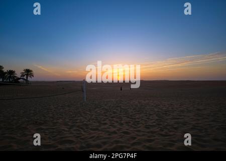 Sonnenaufgang über der Wüste mit Volleyballnetz und früh aufgehenden Menschen. Im Tilal Liwa Hotel Desert Resort nahe Abu Dhabi, Vereinigte Arabische Emirate Stockfoto