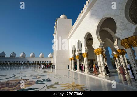 Blick auf den schattigen Wandportiko mit Säulen mit goldenen Palmenstämmen. In der Scheich-Zayid-Moschee in Abu Dhabi, Vereinigte Arabische Emirate, Stockfoto