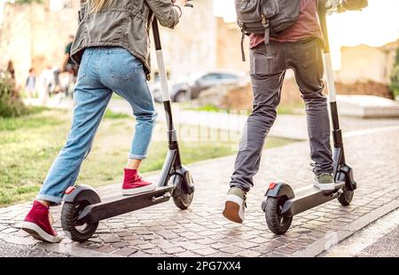 Ein Jahrtausendpaar, das elektrische Roller im städtischen Stadtpark fährt - Genz-Studenten nutzen neue ökologische Transportmittel - umweltfreundliches Energiekonzept Stockfoto