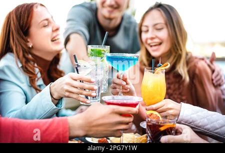 Junge Freunde, die mehrfarbige Fruchtgetränke anstoßen - schicke Leute, die Spaß miteinander haben, Cocktails zur Happy Hour trinken - Essen und Trinken Life Style CO Stockfoto