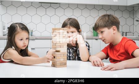 Rücksichtsvolle und konzentrierte Kinder, die das Spiel mit dem Backsteinturm balancieren und Pyramiden auf dem Tisch bauen. Informative ökologische Spiele zu Hause Stockfoto