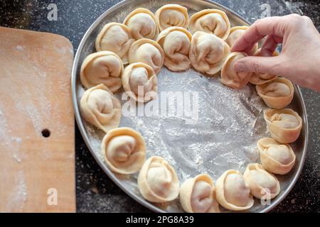 Köstliche Teigtaschen mit Fleisch. Die Frau stellt die Knödel auf ein Tablett. Stockfoto