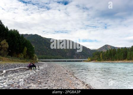 Zwei Freundinnen, jung und alt, sind midi auf einem trockenen Baumstamm auf einem gedämpften Fluss mit einem Steinboden Katun in Sibirien. Stockfoto