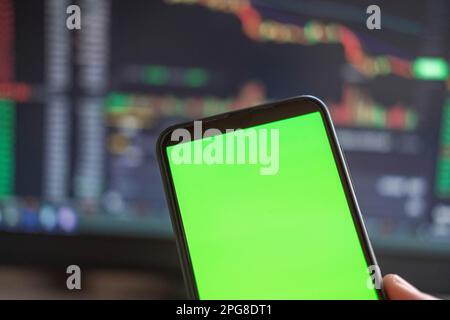 Schwarzes Telefon mit leerem Mockup-Bildschirm auf steigendem Aktiendiagramm. Nahaufnahme-Hand zeigt isoliertes grünes Display des Smartphones. Online-Banking, Nutzung von Fonds-Apps. Fina Stockfoto