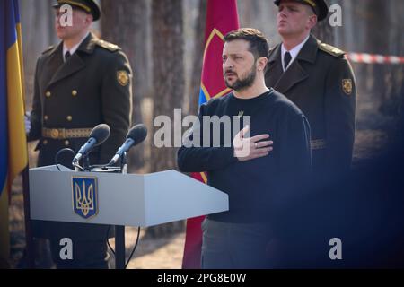 Moschun, Ukraine. 21. März 2023. Der ukrainische Präsident Volodymyr Zelenskyy steht für die Nationalhymne während einer Zeremonie an der Gedenkstätte der Engel des Sieges am 21. März 2023 in Moschun, Oblast Kiew, Ukraine. Kredit: Pool Photo/Pressestelle Des Ukrainischen Präsidenten/Alamy Live News Stockfoto