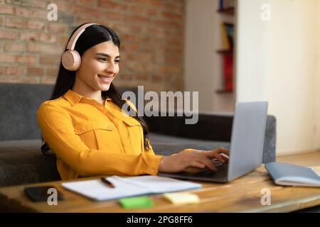 Lächelnde junge spanierin mit kabellosen Kopfhörern und Laptop zu Hause, beim Lernen oder Arbeiten im Internet, freier Platz Stockfoto