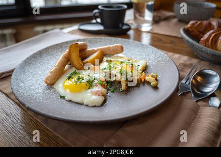 Eine Nahaufnahme mit Wurst, Kartoffel, Rührei auf einem grauen Teller. Traditionelles europäisches englisches Frühstück. Stockfoto