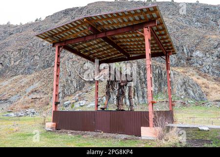 Ein uraltes Skelett eines prähistorischen Tieres steht vor dem Hintergrund von Natur und Bergen. Stockfoto