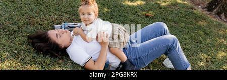 Brünette Mutter schmollt Lippen und liegt auf dem Gras mit einem kleinen Mädchen, Banner, Stock Image Stockfoto