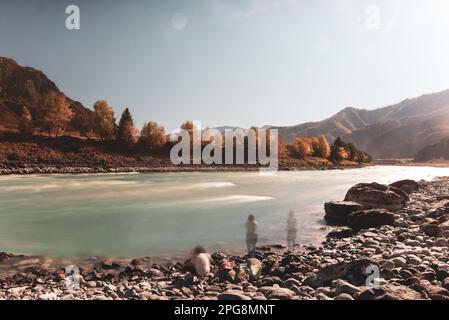 Verschwommene Silhouetten von zwei Frauen, die mit einer Angelrute am Ufer des Bergflusses Katun in Altai zwischen den Felsen am Nachmittag in aut ruhten Stockfoto