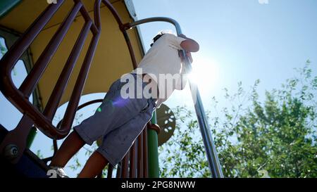 Das Kind rutscht vom Spielplatz an einem wunderschönen sonnigen Tag im Stadtpark herunter. Aktives Kind rutscht mit Leuchteffekt nach unten Stockfoto