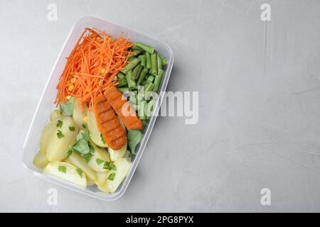 Leckere Kartoffeln mit Schnitzeln und Gemüse in einem Kunststoffbehälter auf einem leichten Tisch, Draufsicht. Platz für Text Stockfoto