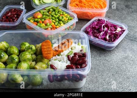 Satz Kunststoffbehälter mit frischen Lebensmitteln auf grauem Tisch Stockfoto