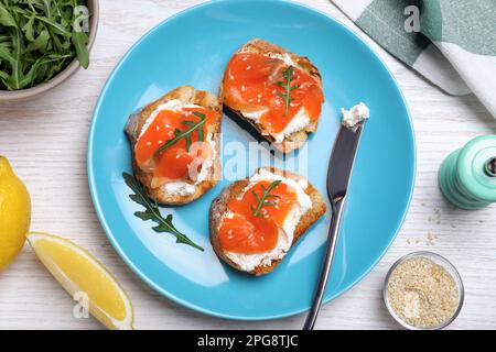 Köstliche Sandwiches mit Frischkäse, Lachs und Rucola, serviert auf einem weißen Holztisch, flach liegend Stockfoto