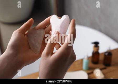 Eine Frau, die Jade und Rosen-Quarz-Gua-Sha-Werkzeuge im Badezimmer hält, Nahaufnahme Stockfoto