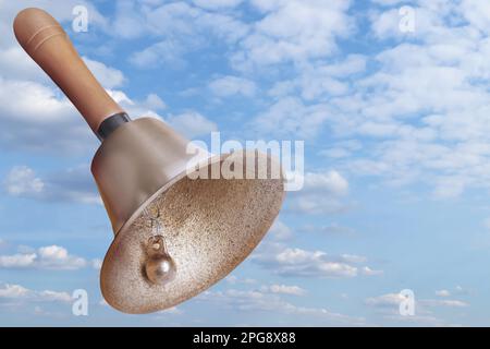 Glänzende Schulglocke mit Holzgriff am blauen Himmel Stockfoto
