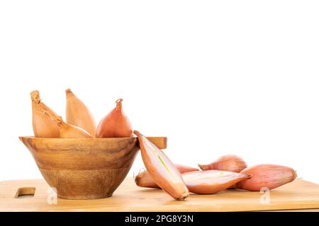 Eine in zwei Hälften geschnittene Bio-Zwiebel und mehrere ganze in einem Holzbecher auf einem Bambustablett, Makro, auf weißem Hintergrund. Stockfoto