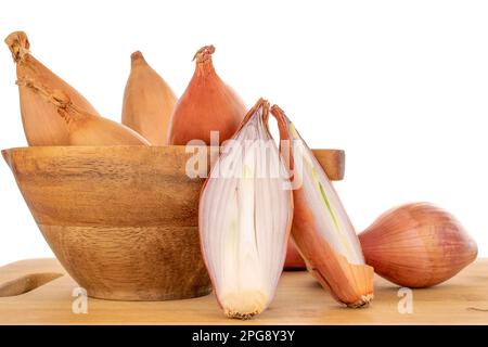 Eine in zwei Hälften geschnittene Bio-Zwiebel und mehrere ganze in einem Holzbecher auf einem Bambustablett, Makro, auf weißem Hintergrund. Stockfoto