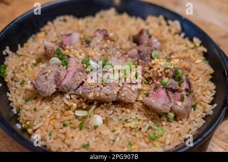 Rindfleisch mit gebratenem Knoblauchreis, ein japanisches Gericht bestehend aus einer Schüssel Reis garniert mit seltenem Rindfleisch, serviert auf einer schwarzen Pfanne Stockfoto