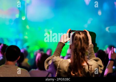 Abstrakte Rückansicht eines Mädchens, das mit seinem Smartphone-Musikkonzert Fotos mit Lichtern, Rauch und vielen Menschen macht Stockfoto