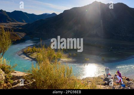 Eine Gruppe von Künstlerinnen malt Landschaftsgemälde auf einer Klippe in der Nähe eines Berges unter der Sonne im Schatten mit dem Fluss Katunya in Altai in der Even Stockfoto