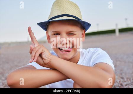 Porträt eines bösen Jungen in einem stylischen Hut. Ein Teenager macht Gesichter, die in die Kamera schauen. Stockfoto