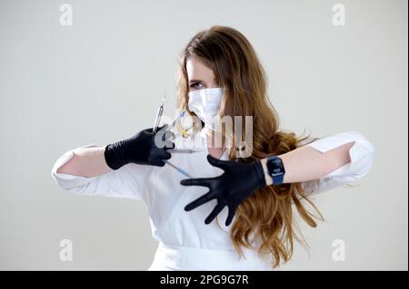 Der Chirurg hält das Skalpell in Schürze und Maske mit hellem Hintergrund. Medizinisches und pharmazeutisches Konzept. Skalpell-Chirurg-Schere, kurz vor der Operation. Verantwortungsvolle Arbeit des Chirurgen. Stockfoto