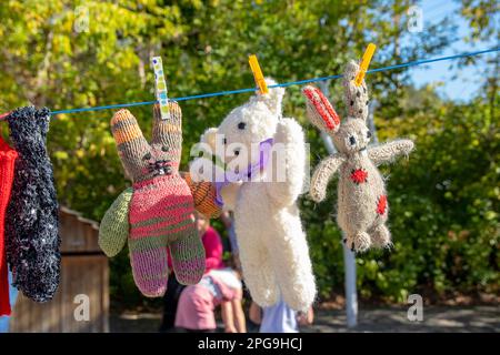 Kinderspielzeug. Handgefertigter weißer Teddybär und flauschige Häschen auf der Wäscheleine auf verschwommenem natürlichen Hintergrund. Mit Wäscheklammern fixiert. Stockfoto