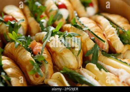 Viele Croissants mit rotem Fisch, Käse und frischem Gemüse werden in einer Pappschachtel geliefert, damit das Catering-Service an einem Veranstaltungsort angeboten wird Stockfoto