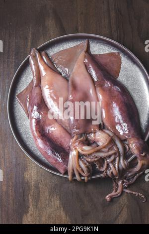 Rohe Kalmare auf grauen Platten mit Koriander und Zitronen. Auf dunklem Holzhintergrund. Draufsicht Stockfoto