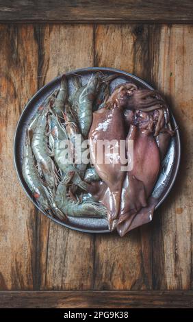 Rohe Meeresfrüchte. Frische Garnelen und Tintenfische auf grauem Teller. Holzhintergrund. Stockfoto