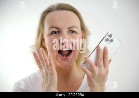 Überraschte Frau benutzt ein Smartphone, sitzt auf dem Sofa, Blick nach vorne, isoliert. Hochwertiges Foto Stockfoto