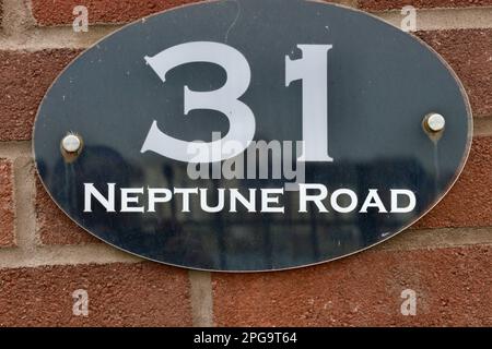 Straßennamen, Hausnummern und Handelsschilder in Großbritannien. Nummer 31 und Straßenname Neptune Road in Weiß auf schwarzem Hintergrund Stockfoto