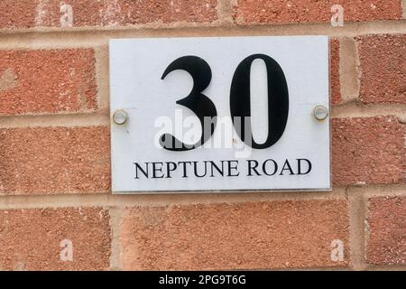 Tür Nummer 30 und Straßenname Neptune Road in Schwarz auf weißem Hintergrund an einer Ziegelwand. Stockfoto