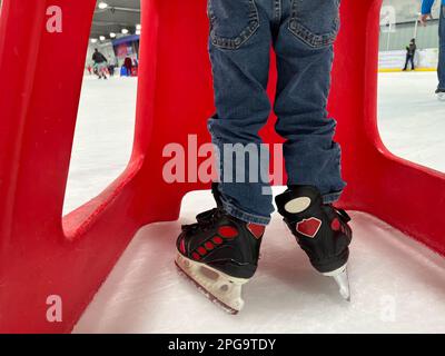 Einsteiger-Schlittschuhläufer mit einem Plastikläufer zur Unterstützung. Stockfoto