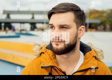 Porträt in einem stilvollen, lässigen jungen Freiberufler, der mit einem modernen Laptop arbeitet und im Skateboard-Park im Freien auf einem Smartphone verwendet Stockfoto