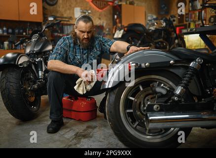 Bärtiger reifer Motorradputzer in Garagenarbeitsplätzen Stockfoto