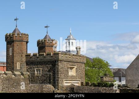 Sonniger Frühlingstag Stadtzentrum von Antrim, Schlacht und Steinfassade der Barbican Gate Lodge mit Turm des ehemaligen Gerichtsgebäudes von Antrim im Hintergrund Stockfoto