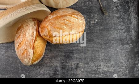 Zwei knusprige Brotlaibe auf rustikalem Hintergrund mit einem Bannetonkorb. Draufsicht Stockfoto