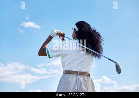 Rückansicht einer schwarzen jungen Frau, die Golf gegen blauen Himmel spielt, Kopierraum Stockfoto