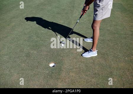 Minimale Aufnahme aus einem großen Winkel, wie eine Frau Golf spielt, bei Sonnenlicht und Ball auf Loch zielt, Kopierraum Stockfoto