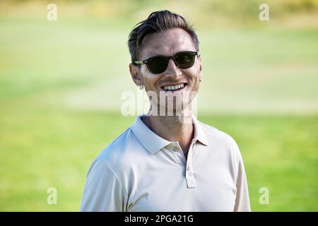 Porträt eines lächelnden Weißen mit Sonnenbrille im Sommer auf grünem Feld Stockfoto