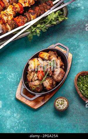 Grillfleisch - Schweinefleisch, Huhn und Gemüse auf einer gusseisernen Pfanne. Gegrillte Spieße auf blauem Holzhintergrund. Draufsicht Stockfoto