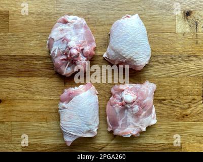 Vier Hähnchenschenkel mit Haut auf der hölzernen Arbeitsfläche, Draufsicht Stockfoto