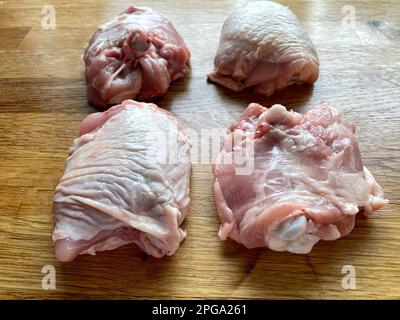 Vier Hähnchenschenkel mit Haut auf der hölzernen Arbeitsfläche, Seitenansicht. Stockfoto